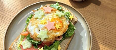 A sandwich with various toppings on a plate, accompanied by a cup of coffee on a wooden table.