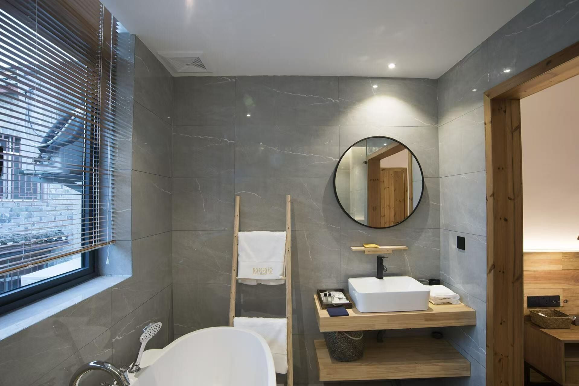 Un baño moderno con una bañera independiente, un espejo redondo y un estante de madera con artículos de aseo.