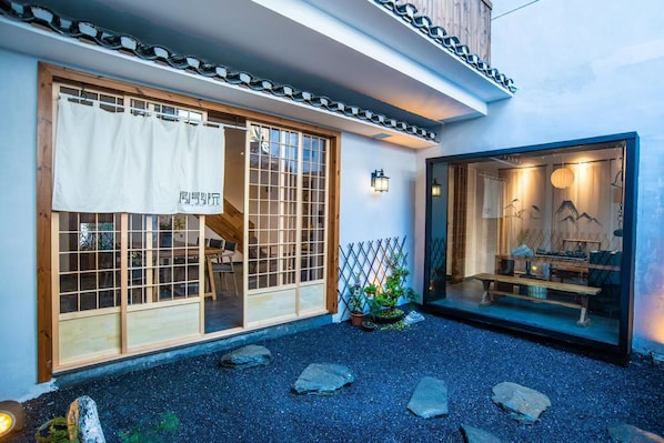 A traditional Japanese-style building with sliding doors, a small garden with rocks and plants, and a seating area with tables and chairs.