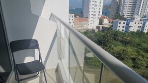 Een balkon met glazen hekwerk, twee zwarte stoelen en uitzicht op een stadsgezicht met gebouwen en groen.