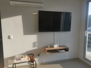 A room with a mounted TV, a small wooden shelf, a desk with a chair, and a window. - Family apartment close to the beach in Rodadero Sur (Gaira)