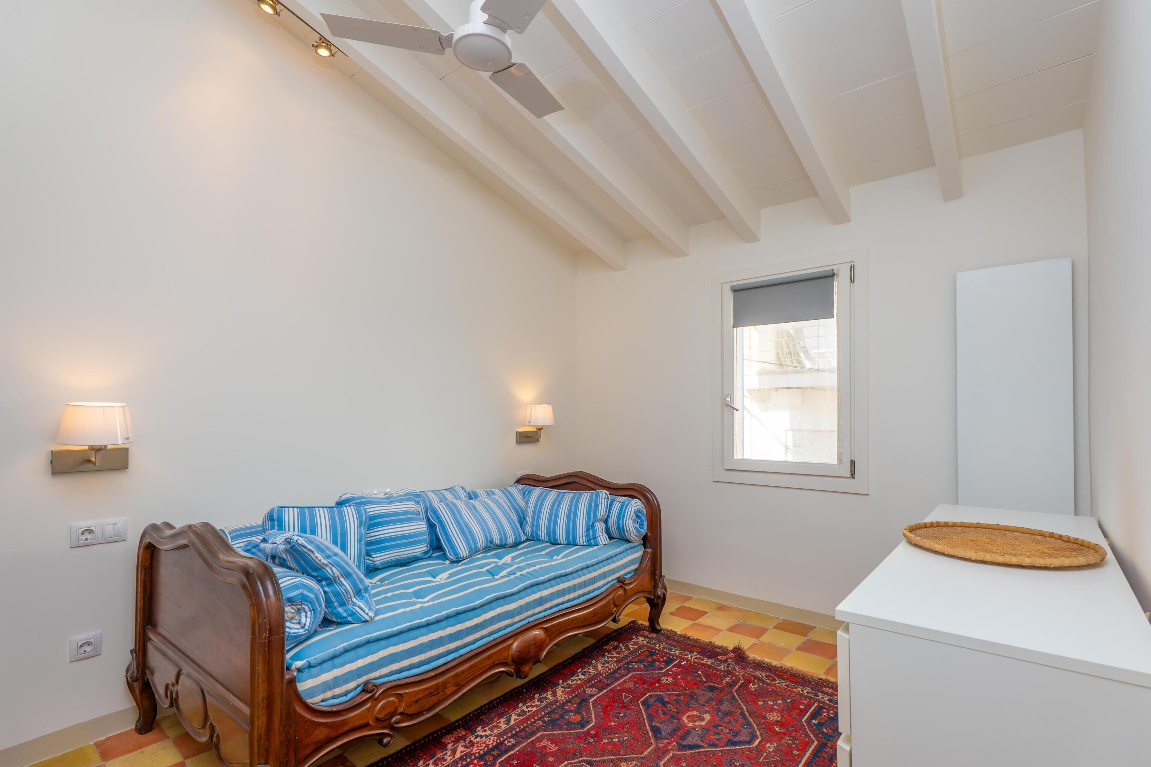 Un dormitorio con una cama, ventilador de techo, ventana y una mesita.