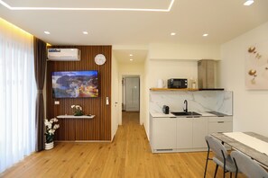 A modern living room with a flat-screen TV, wooden panel wall, and a dining area with a kitchen in the background. - La Dimora Azzurra 101, Vlore, Albania (Vlore)