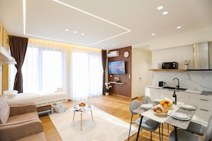 A modern living room with a sofa, a dining table set for two, and a kitchen area with a microwave and a TV. - La Dimora Azzurra 101, Vlore, Albania (Vlore)