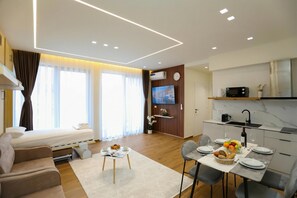 A modern hotel room with a sofa, a dining table set for two, a kitchen area, and a TV mounted on the wall. - La Dimora Azzurra 101, Vlore, Albania (Vlore)