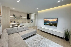 A modern living room with a sectional sofa, a flat-screen TV mounted on the wall, and a kitchen in the background. - La Dimora Azzurra 601, Vlore, Albania (Vlore)