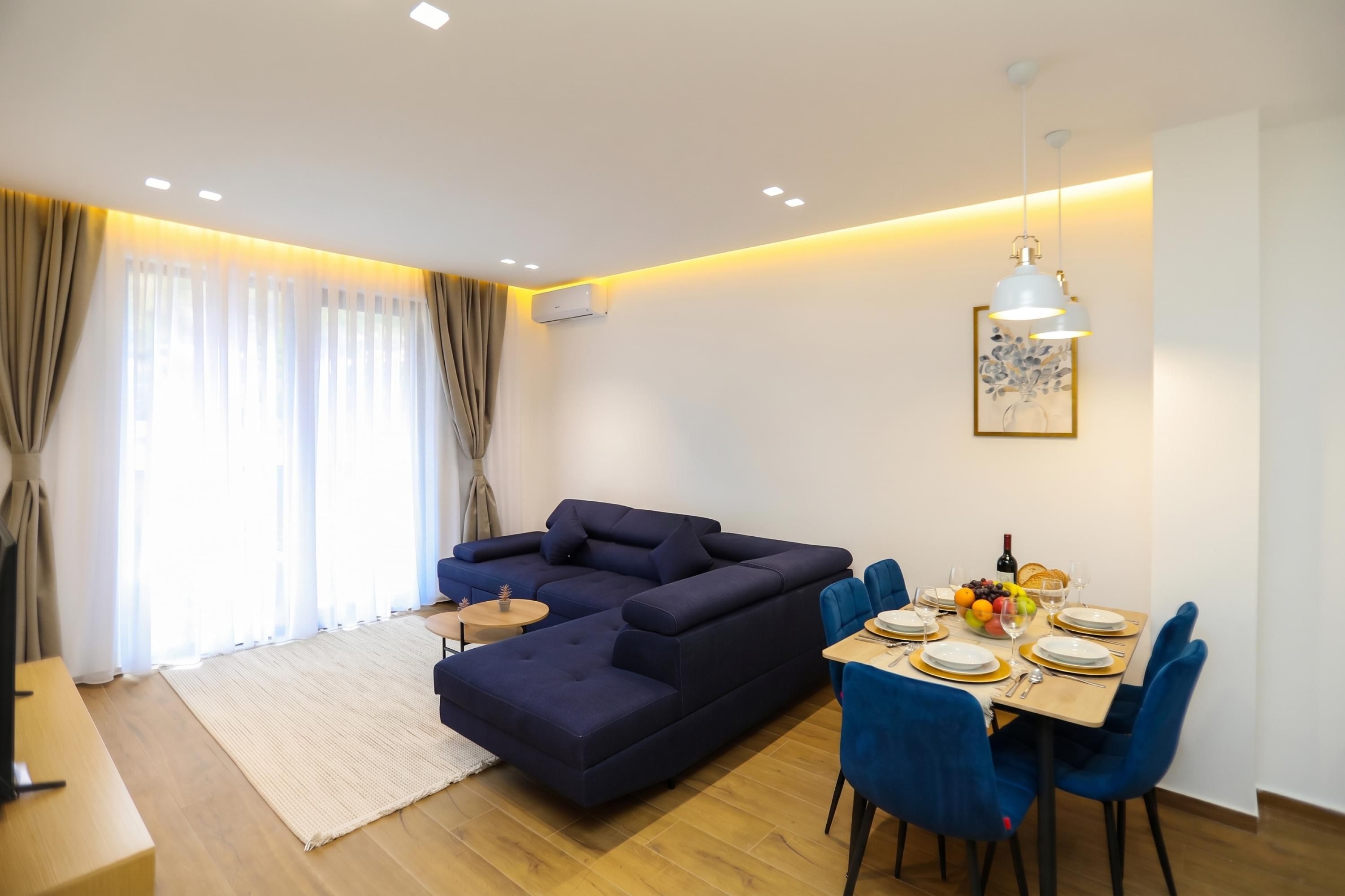 A modern living room with a dark blue sofa, a dining table set for four, and a small side table.