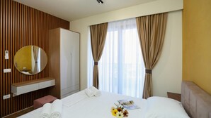 Une chambre d’hôtel comprenant un lit, une table de chevet, un miroir, une armoire et une fenêtre avec des rideaux.