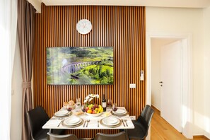 Ein Essbereich mit einer Wand aus Holzpaneelen, einem angebrachten Fernseher, der eine Landschaft zeigt, und einem für eine Mahlzeit gedeckten Tisch.