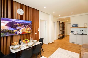 A modern dining area with a flat-screen TV, wooden panel wall, and a view of a coastal town. - La Dimora Azzurra 902, Vlore, Albania (Vlore)