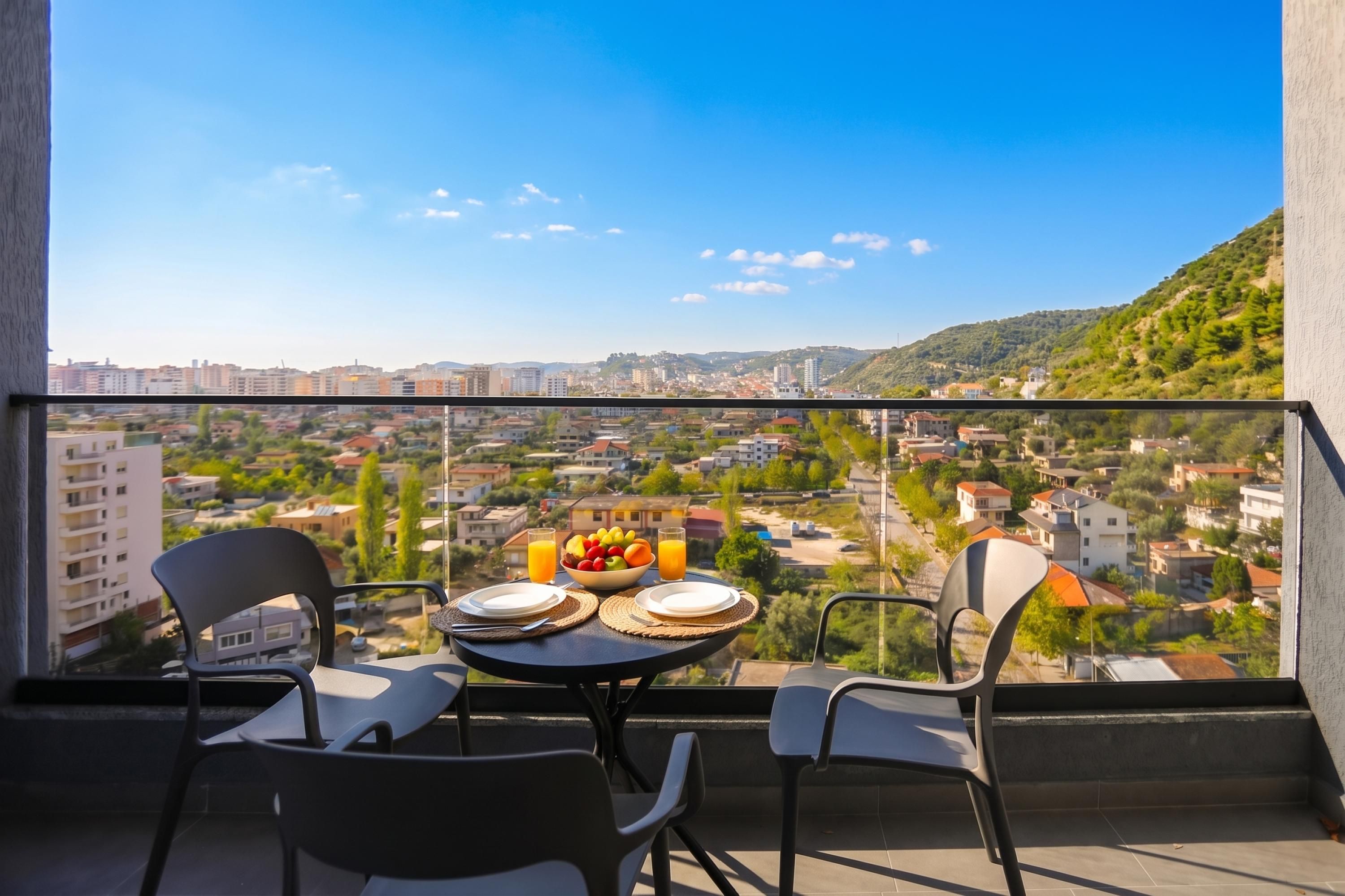 A balcony with a table set for two, overlooking a cityscape with buildings and greenery.