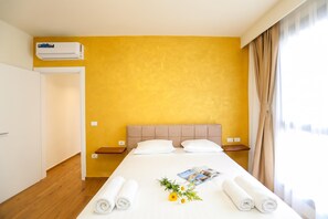 A hotel room with a bed, a bedside table, a nightstand, an air conditioning unit, and a window with curtains. - La Dimora Azzurra 901, Vlore, Albania (Vlore)
