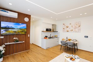 Eine moderne Küche mit Einbauherd, ein Essbereich mit Tisch für zwei Personen und ein Fernseher, der an einer Wand aus Holzpaneelen befestigt ist.