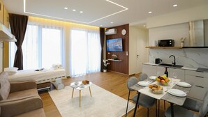 Habitación de hotel moderna con cama, sofá, mesa de comedor y área de cocina.