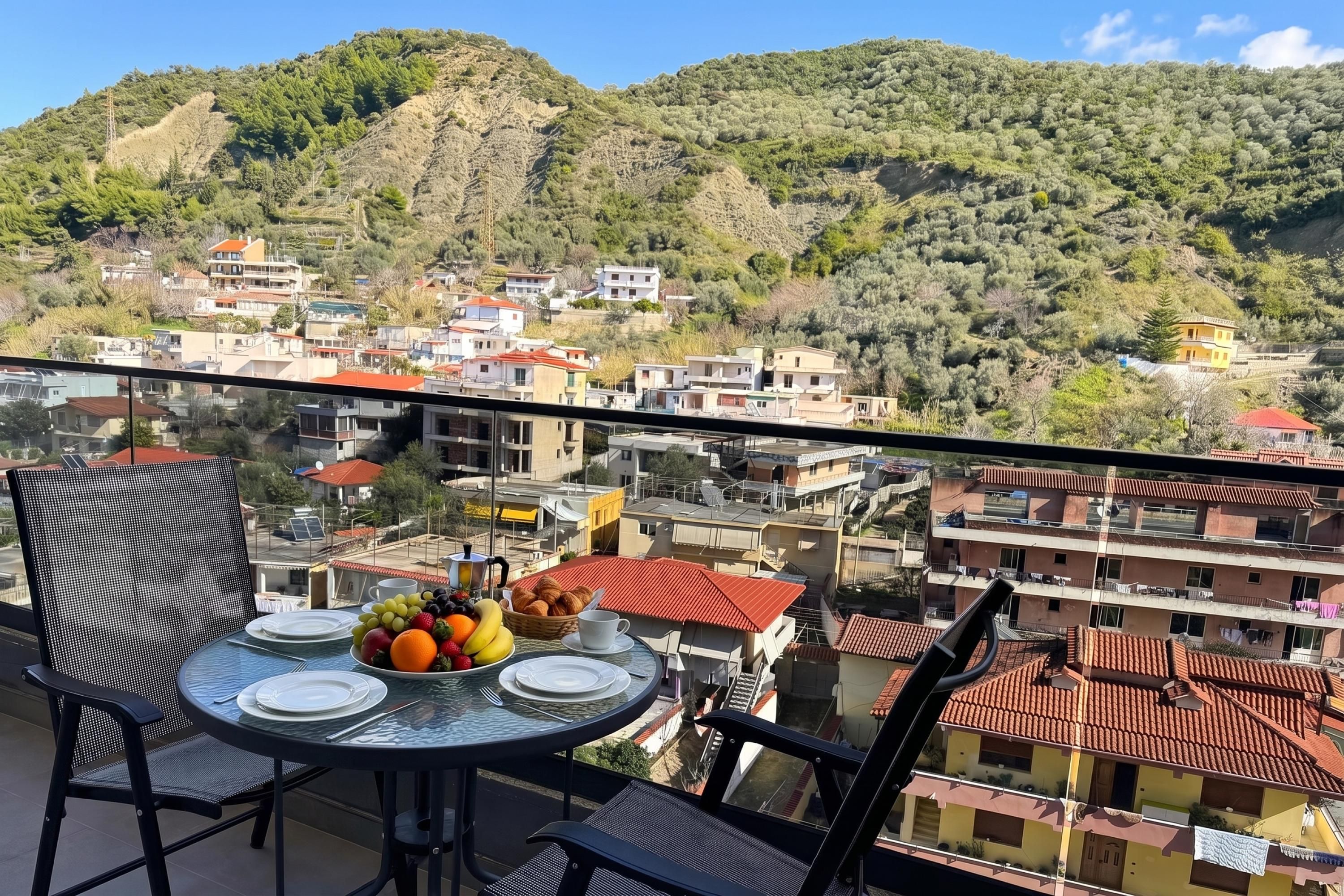 A balcony with a table set for two, overlooking a hillside with buildings.