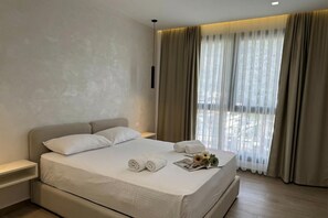 A modern hotel room with a large bed, a bedside table, a nightstand, and a window with sheer curtains. - La Dimora Azzurra 501, Vlore, Albania (Vlore)