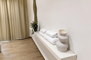 A bathroom with a wooden floor, a white shelf with towels and a vase, and a plant. - La Dimora Azzurra 501, Vlore, Albania (Vlore)