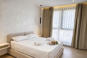 Une chambre d’hôtel avec un grand lit, une table de chevet, une commode, une fenêtre avec des rideaux et une vue sur l’extérieur.