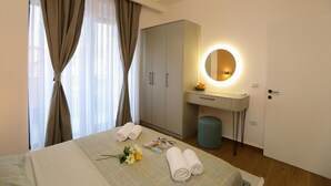 Quarto de hotel com cama, escrivaninha com espelho, guarda-roupa e mesa de cabeceira.