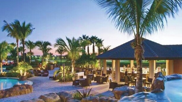 Zwembadgedeelte van een resort met een fontein, palmbomen en buitentoegenlijke zitplaatsen.