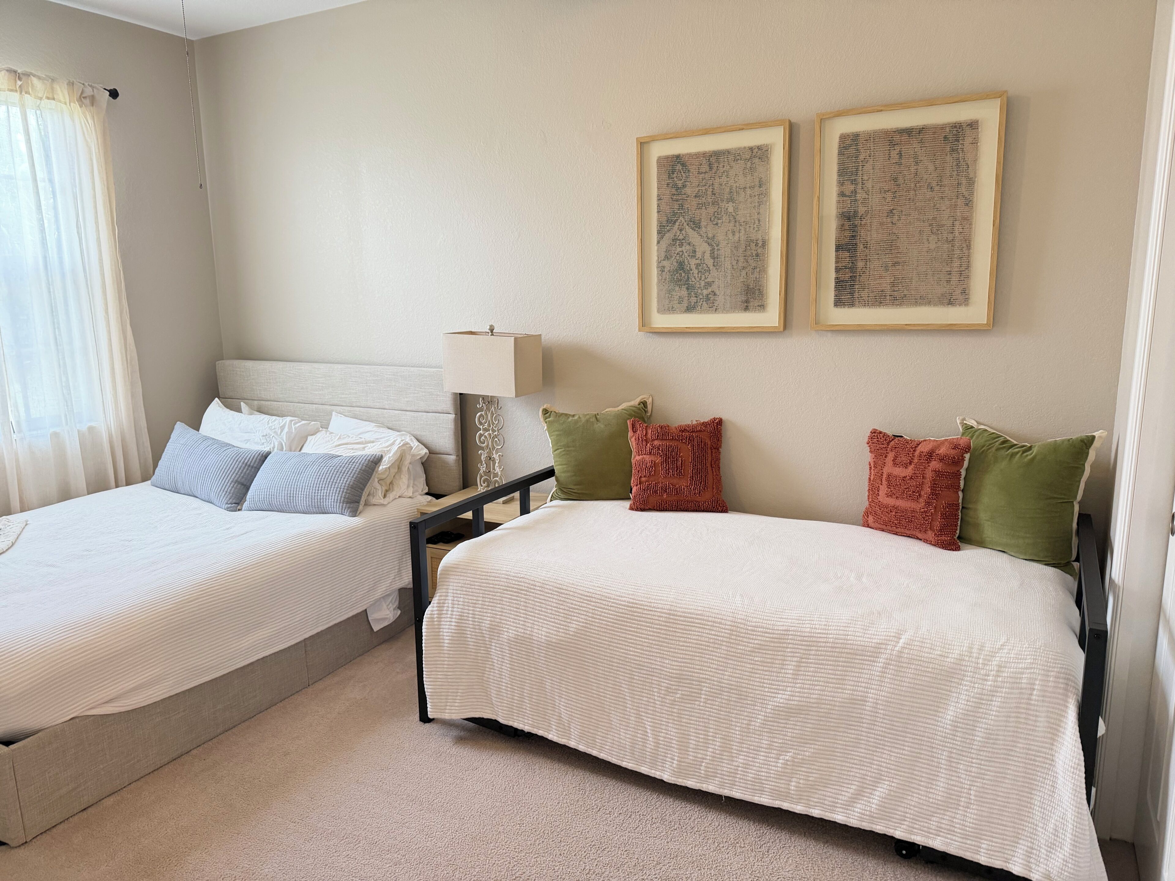 A hotel room with two beds, a nightstand, a lamp, and two framed pictures on the wall.