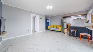 Ein modernes Wohnzimmer mit einer Couch, einer Küchenzeile mit Kühlschrank und einem Essbereich mit Hockern.
