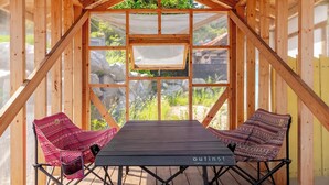 Eine hölzerne Struktur mit einem Tisch und zwei stuhlförmigen Sitzgelegenheiten, mit Blick auf Felsen und Grün.