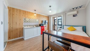 A compact room with a wooden floor, a kitchenette with a red appliance, a bed with a blue headboard, and a window with curtains. - Yangyang Yellowstop Pet-friendly Pension (Yangyang)