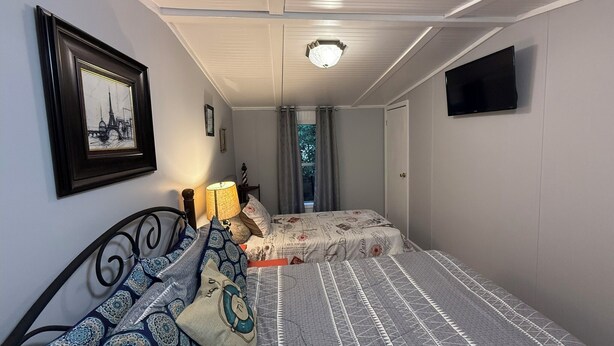 Een slaapkamer met twee bedden, een plafondventilator, een televisie en een lijst met een afbeelding aan de muur.