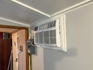 A room with a white air conditioning unit mounted on the wall, a door with a wooden frame, and a wall-mounted electrical panel. - Cozy 1-bedroom mobile home in terrific North Augusta with AC (North Augusta)