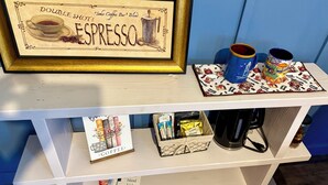 Een lijst met een bord waarop staat 'DOUBLE SHOT! SOHO COFFEE BAR Blend ESPRESSO', een koffiezetapparaat, twee mokken en een koffie-placemat op een witte plank.