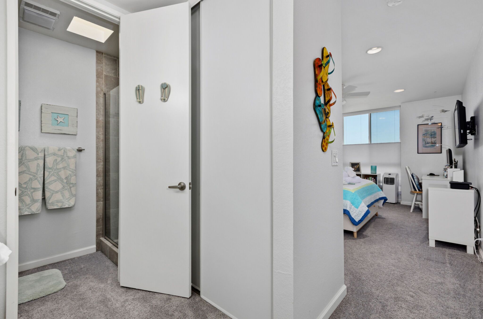 Une chambre d’hôtel moderne équipée d’une douche, d’un lit avec une couvre-lit à rayures bleues et blanches, d’un bureau avec une chaise et d’un téléviseur.