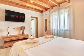Habitación de hotel con una cama, un aparador de madera, un televisor mostrando 'NETFLIX', un espejo y una ventana con cortinas.