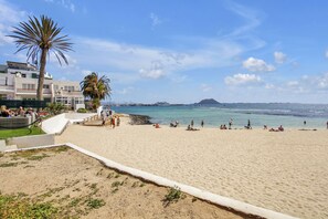 Une plage avec des gens, un palmier et un bâtiment en arrière-plan.