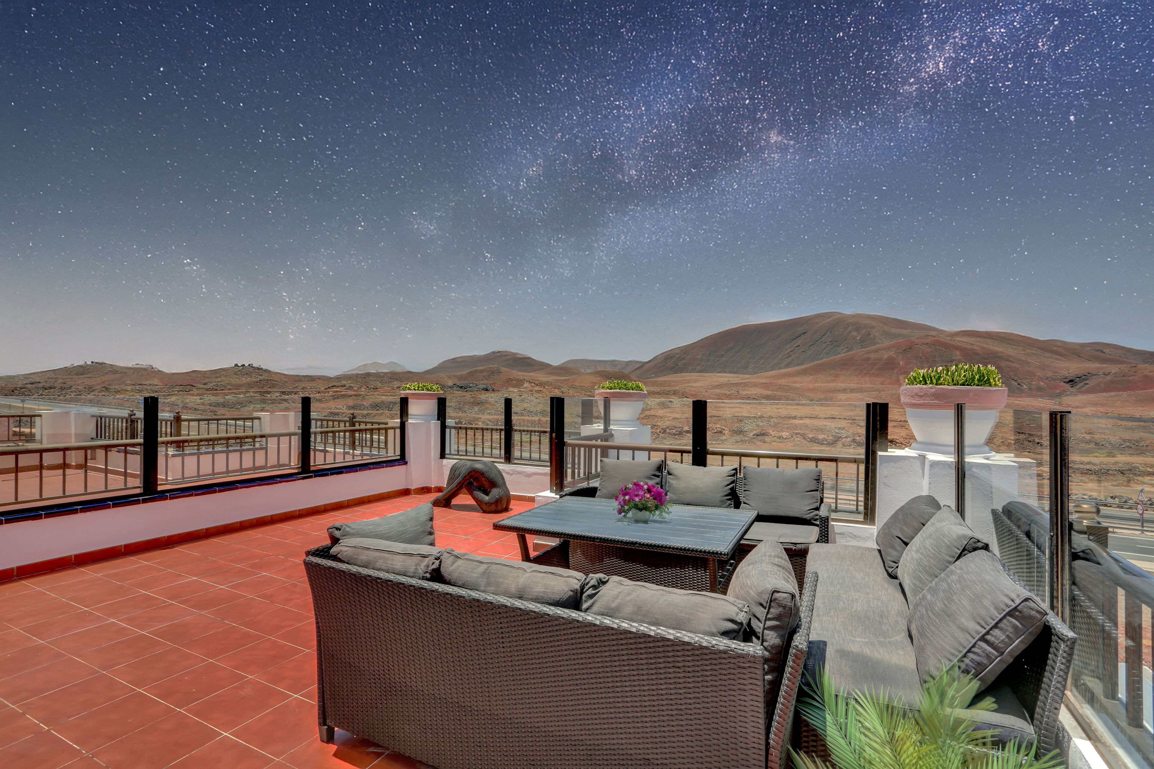 Una terraza en la azotea con mobiliario exterior, vista al paisaje desértico y cielo estrellado.