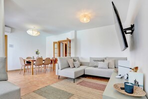 Un salon moderne comprenant un canapé, une table à manger, des chaises et un téléviseur fixé au mur.