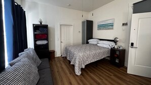 Quarto com cama, sofá, guarda-roupa, ventoinha no teto e porta.