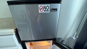 Uma geladeira compacta com um aviso de 'Proibido Fumar', um adesivo 'Magic Chef' e interior transparente.