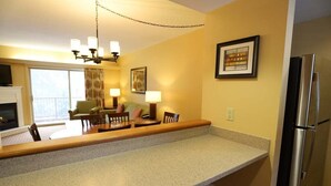 Una cocina con encimera de granito, refrigerador de acero inoxidable, comedor con mesa y sillas, y una araña.