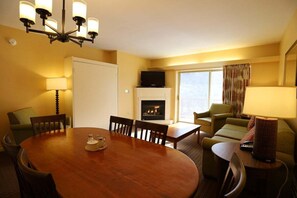 Une chambre d’hôtel équipée d’une table à manger, de chaises, d’un canapé, d’une télévision, d’une cheminée et d’une fenêtre avec des rideaux.