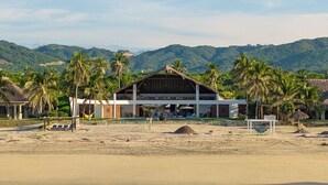 A beachfront hotel with a thatched-roof structure, a pool, and palm trees. - Casa STÁA OCEANFRONT PUERTO ESCONDIDO, PRIVACY OCEANFRONT HOUSE (SANTA MARIA COLOTEPEC)