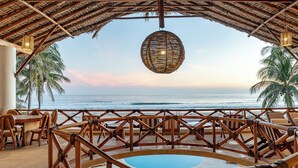 A beachside lounge with a pool, wooden furniture, and a thatched roof. - Casa STÁA OCEANFRONT PUERTO ESCONDIDO, PRIVACY OCEANFRONT HOUSE (SANTA MARIA COLOTEPEC)