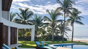 A poolside area with lounge chairs and a pool, surrounded by palm trees and a view of the ocean. - Casa STÁA OCEANFRONT PUERTO ESCONDIDO, PRIVACY OCEANFRONT HOUSE (SANTA MARIA COLOTEPEC)