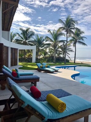 A poolside area with lounge chairs and a pool, surrounded by palm trees and a view of the ocean.