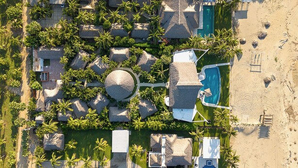 An aerial view of a resort with multiple thatched-roof structures, a central circular building, a swimming pool, and a beach area. - Casa STÁA OCEANFRONT PUERTO ESCONDIDO, PRIVACY OCEANFRONT HOUSE (SANTA MARIA COLOTEPEC)