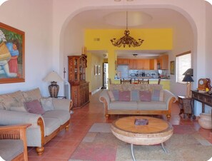 Ein Wohnzimmer mit Sofa, Sessel und Couchtisch, ein Essbereich mit Tisch und Stühlen sowie eine Küche im Hintergrund.
