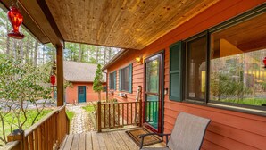 Un patio in legno con una sedia, una casa rossa sullo sfondo e una vista aperta sugli alberi circostanti.