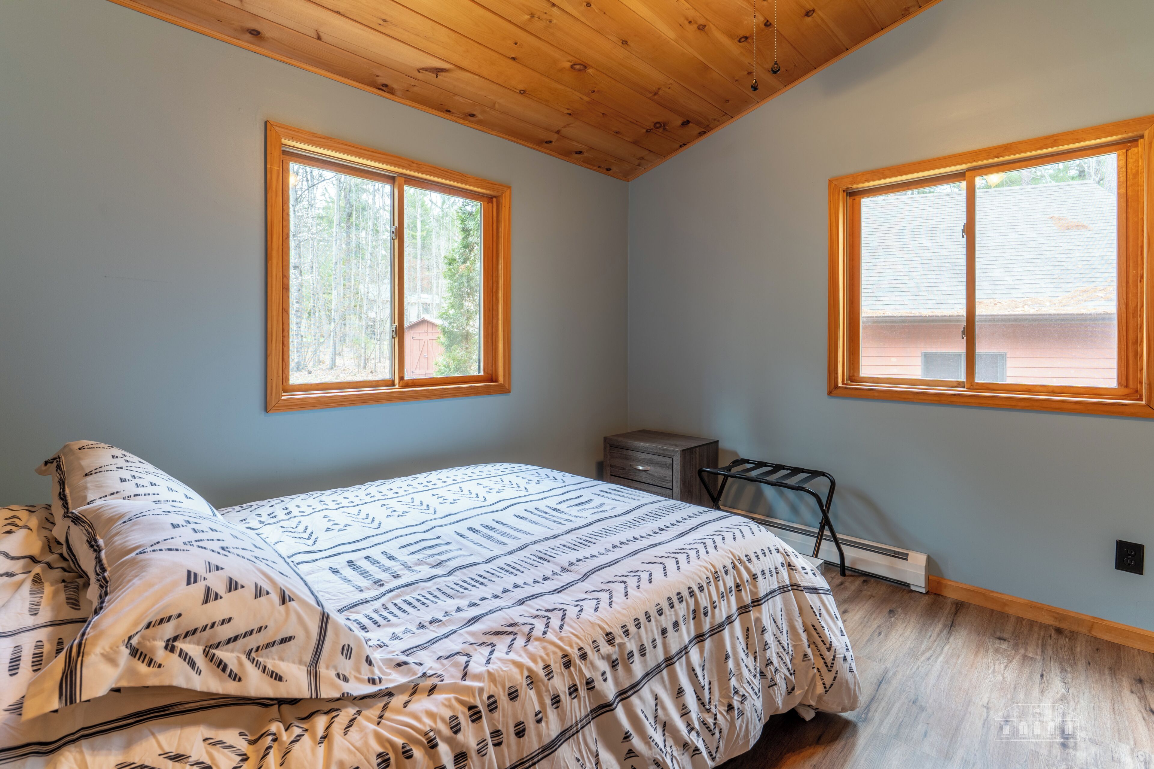 Una camera da letto con un letto, due finestre, un termosifone e un soffitto in legno.