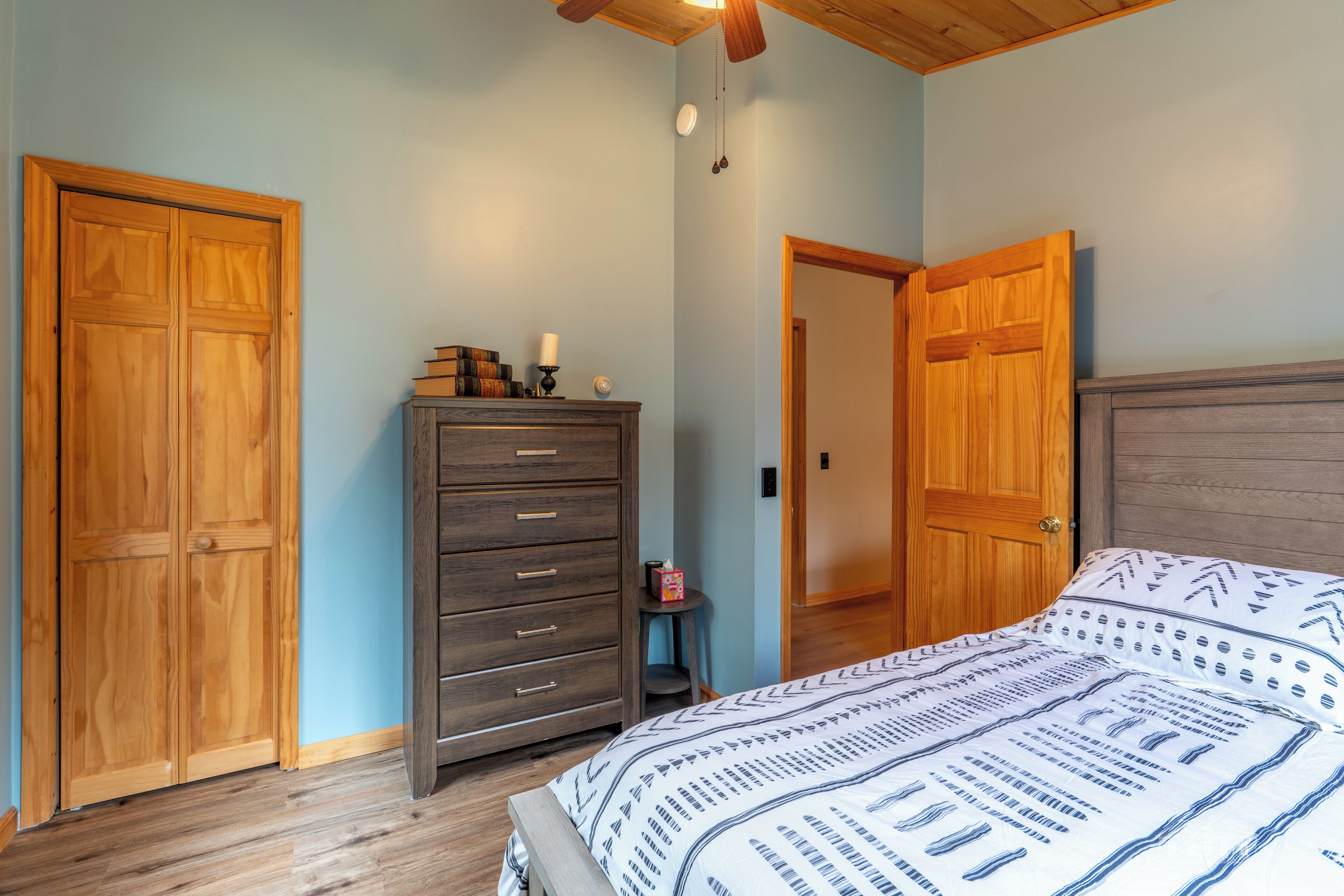 A bedroom with a bed, wooden wardrobe, dresser, and a door leading to another room.