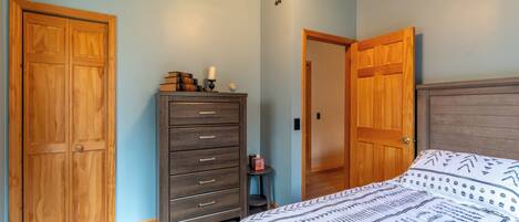 A bedroom with a bed, wooden wardrobe, dresser, and a door leading to another room.